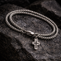 Silver chain bracelet with a cross pendant on a dark stone surface
