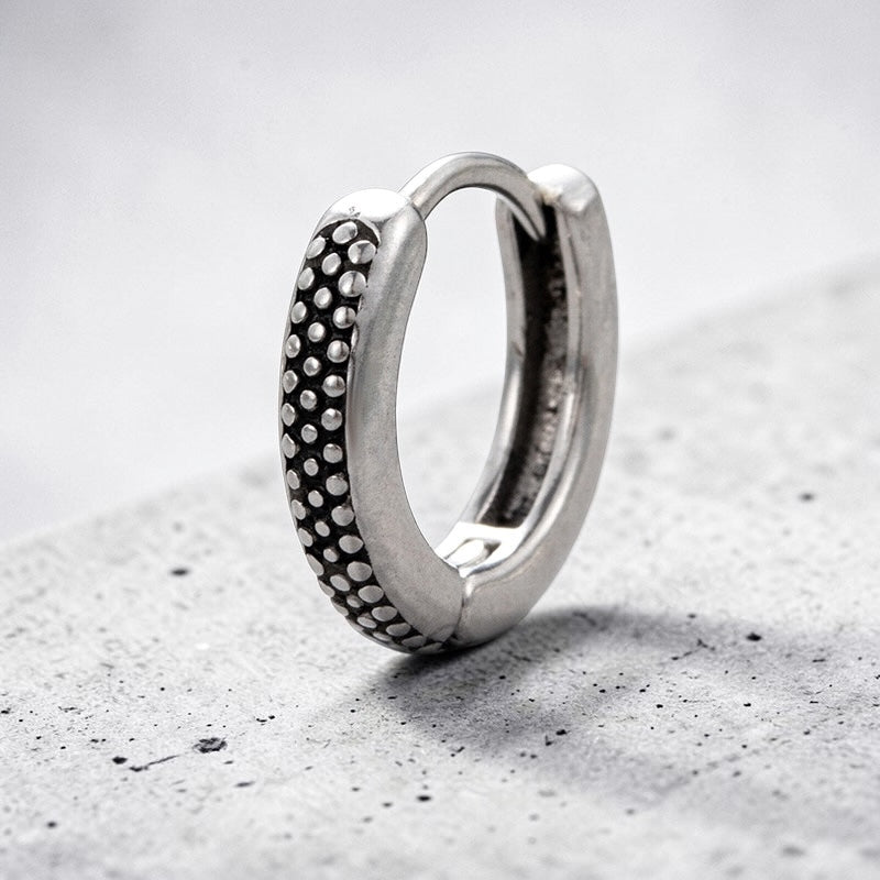 Silver hoop earring with textured design on a gray surface