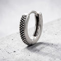 Silver hoop earring with textured design on a gray surface