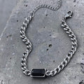 Silver chain bracelet with a black stone on a gray concrete surface