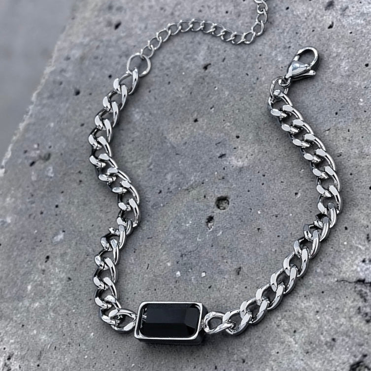 Silver chain bracelet with a black stone on a gray concrete surface