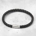 Black braided leather bracelet with a silver clasp on a light gray background