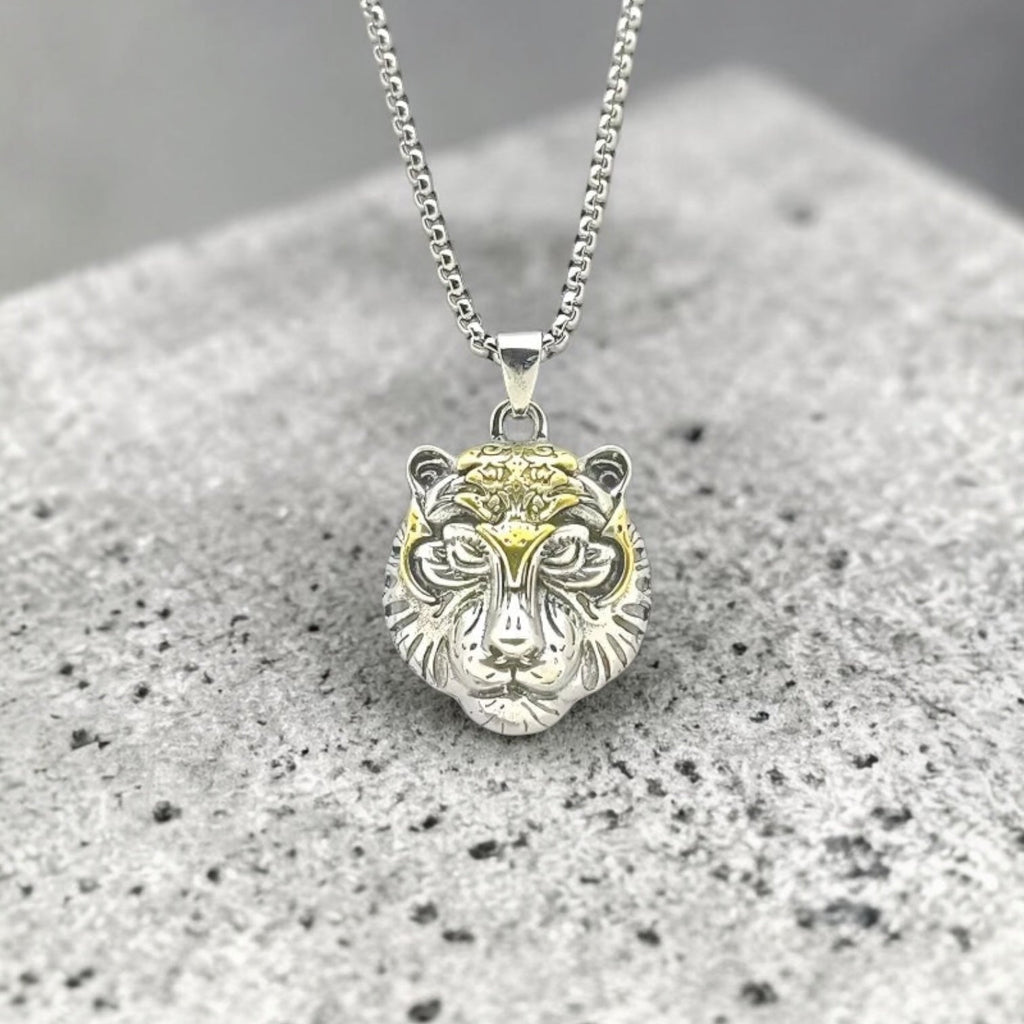 Silver and gold lion head pendant on a chain against a gray background