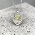 Silver and gold lion head pendant on a chain against a gray background