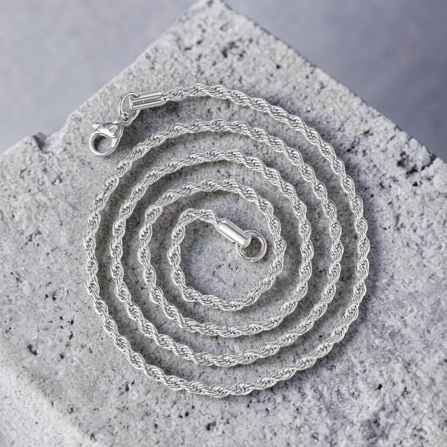 Silver necklace coiled on a textured stone surface