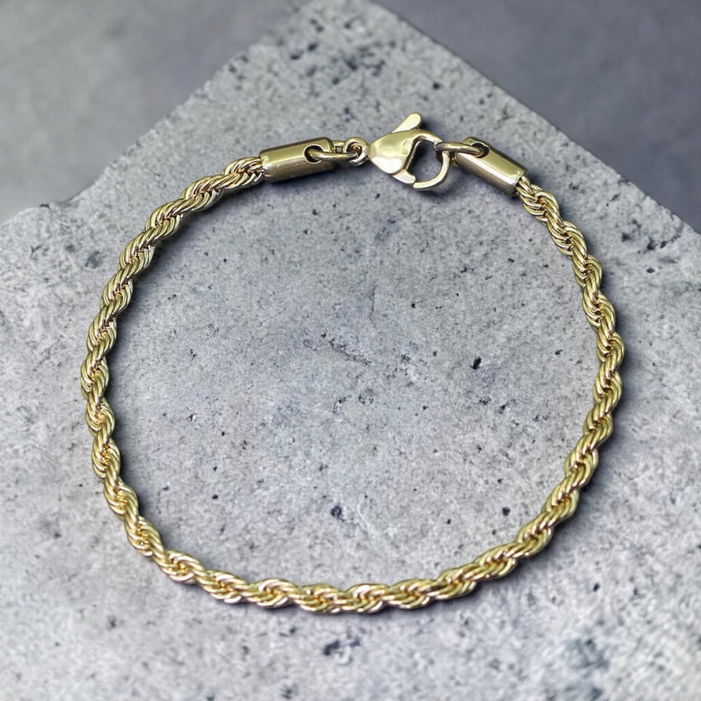 Gold rope chain bracelet on a gray concrete surface