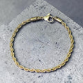 Gold rope chain bracelet on a gray concrete surface