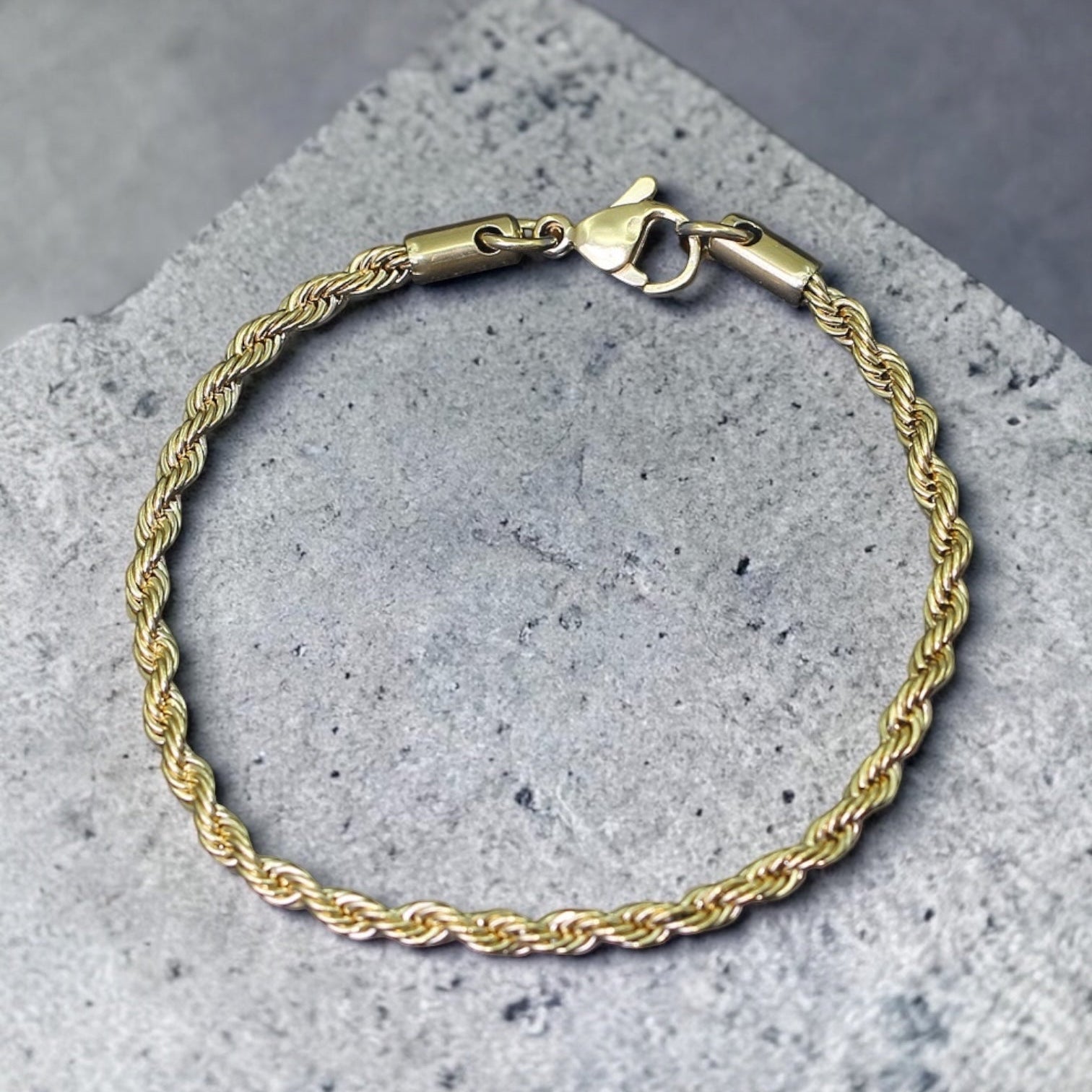 Gold rope chain bracelet on a gray concrete surface